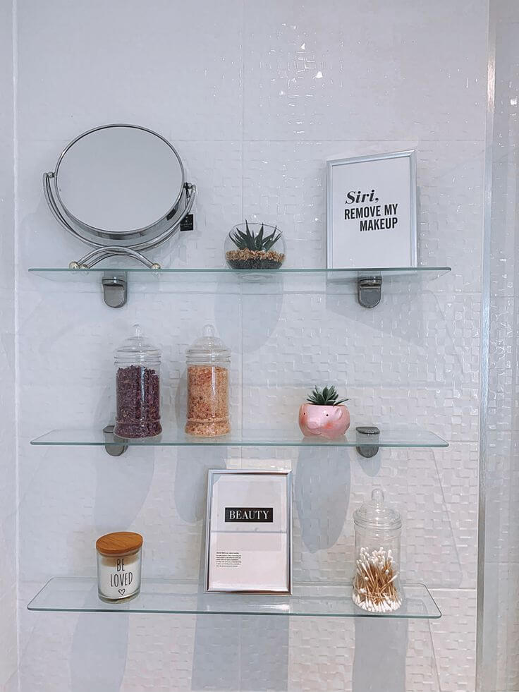 Repisa de cristal en baño moderno con espejo, plantas y artículos de belleza organizados, creando un espacio ordenado y estilizado.